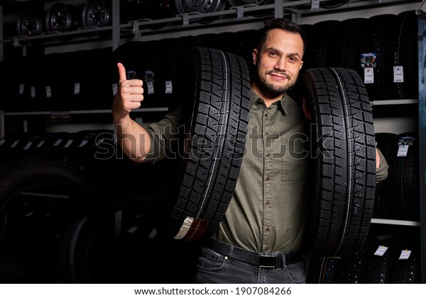 male customer is satisfied with purchase of tyre in\
automobile repair garage, stand holding rubber for car in hands,in\
auto store shop