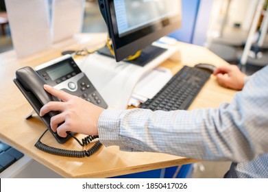 Male customer support operator hand trying to response customer call by using landline phone on working desk in office. Call center business concept