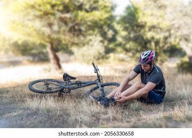 Male Cyclist In An Accident In The Countryside. A Young Cyclist Lying On The Ground After Suffering A Fall From His Bicycle In Which He Injured His Ankle. At Least He Wearing His Helmet