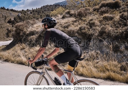 Male cyclist is conquering the challenging uphill terrain on his gravel bike.Sportsman training hard on bicycle in the mountains.Man cyclist  wearing cycling kit and helmet.Beautiful motivation image