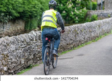 A male cyclist rides a bike in full safety gear - Helmet, high visibility jacket, bike lights