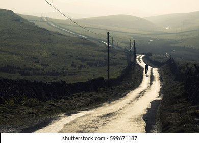 Male Cyclist Rides Down A Wet Winter Road In The Yorkshire Dales, UK