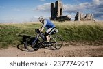 A male cyclist rides his bike along a gravel track passed the Church of St James in Norfolk England in the UK