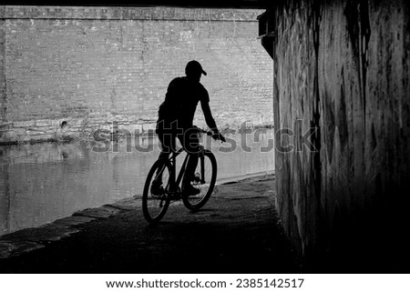 A male cyclist is silhouetted against a brick wall as he rides beneath a bridge along a narrow canal, Huddersfield, Yorkshire, England, UK.