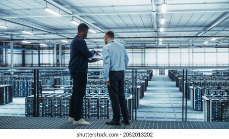 Male Data Center System Administrators and African American IT Specialists Talk, Use Laptop. Information Technology Engineers work on Cyber Security Network Protection in Cloud Computing Server Farm. - Powered by Shutterstock