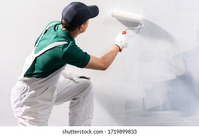 Male decorator painting a wall with white color.