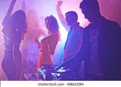 Male Deejay And Dancing Friends Enjoying Night Party