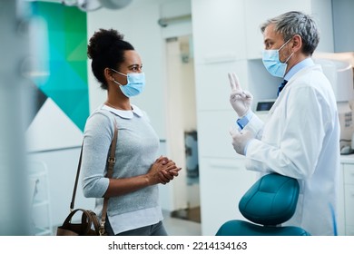 Male Dentist And Black Woman Wearing Face Masks While Talking At Dental Clinic.