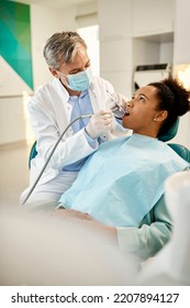 Male Dentist Examining Teeth Of African American Woman At Dental Clinic. 