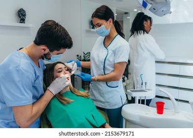 Male dentist with a help of his assistant fixing teeth of a woman patient in the dentists chair. Dentist examining patient teeth and having a dental checkup at dental clinic. - Shutterstock ID 2153679171