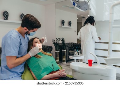Male dentist with a help of his assistant fixing teeth of a woman patient in the dentists chair. Dentist examining patient teeth and having a dental checkup at dental clinic. - Powered by Shutterstock
