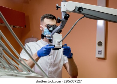 A Male Dentist Looks Into A Microscope. Modern Dentistry Using New Technologies.