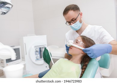 Male Dentist Putting Inhalation Sedation Mask On A Young Girl In Dental Chair, Copy Space