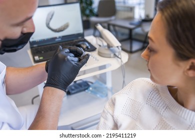 Male dentist showing at invisible braces aligner and talking to his female patient - Shutterstock ID 2195411219
