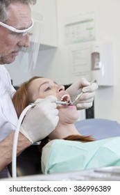 A male dentist treating a female patient - Shutterstock ID 386996389