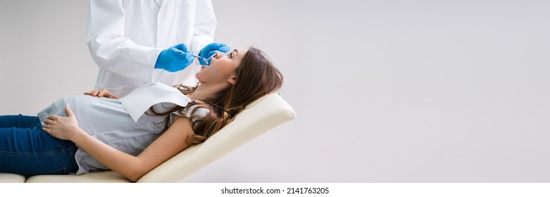 A Male Dentist Treating Teeth Of Young Pregnant Woman Patient Lying In Clinic