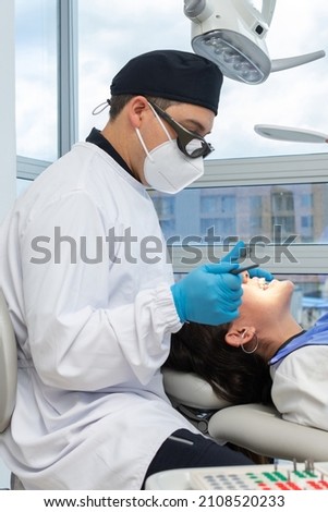 Male dentist in uniform and face mask during a dental intervention on a woman. Dental clinic concept