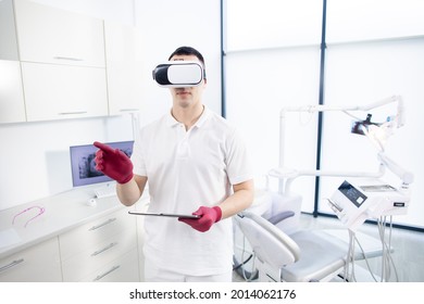 A Male Dentist In Uniform With Special Device In Front Of His Eyes Checks The Digital Image Before The Patient's Visit. The Latest Technologies In Dentistry, 3D Images, Virtual Reality