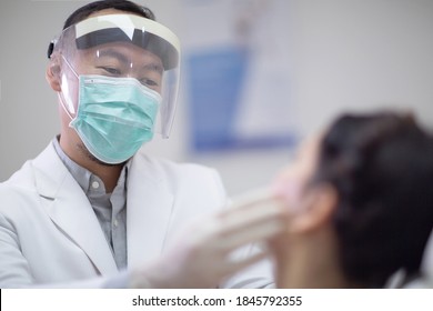 Male Dentist Wearing Face Mask, Gloves And Protective Visor Shiled As Coronavirus Safety Precaution. Young Woman On Dental Checkup Appointment. New Normal And Healthcare Concept