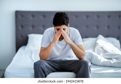 Male depression. Unhappy arab man sitting on bed and thinking about problems, closing face with hands