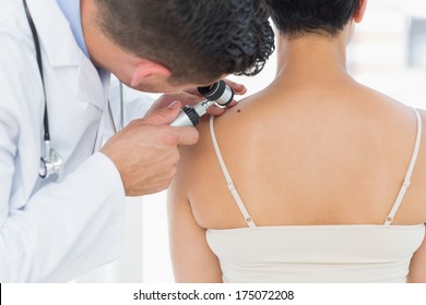 Male Dermatologist Examining Mole On Back Of Woman In Clinic