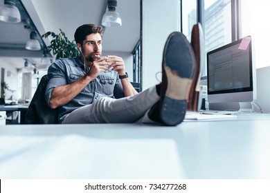 Male designer listening music with cup of coffee. Young man drinking coffee during break in office.