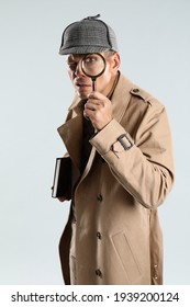 Male detective looking through magnifying glass on grey background