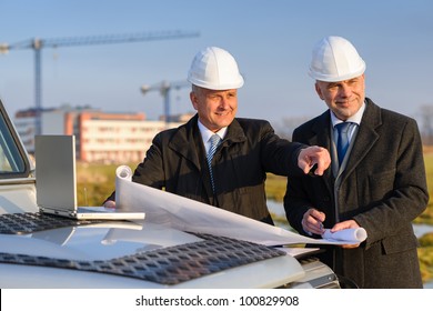 Male developers with blueprints at  construction site discuss architect project