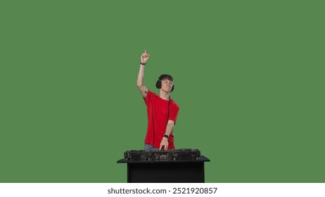 A male DJ wearing a red t-shirt performs at a DJ desk in a studio with a green screen chroma key - Powered by Shutterstock