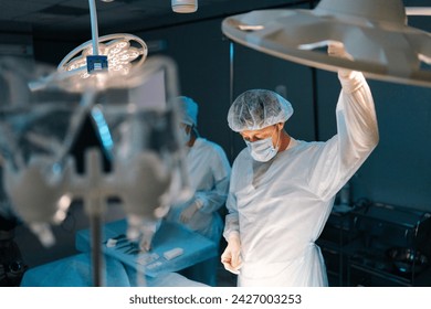 Male doctor adjusting light performing operation in medical gown. Surgical operation by professional surgeons. Surgeon adjusting surgical lamp before operation. Concept of emergency. - Powered by Shutterstock