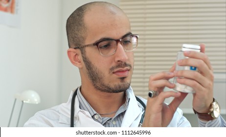 Male Doctor Attentively Reading Medicine Label Of A Bottle Of Pills