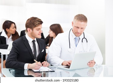 Male doctor and businessman discussing over laptop at desk in office