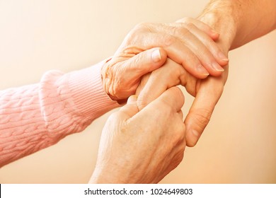 Male doctor care giver holding hands of elderly pensioner woman patient, reassuring in nursing home. Adult man, son carefully helping old mother to get up. Background, close up, copy space, overhead.
