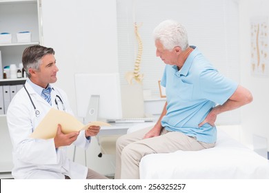 Male Doctor Discussing Reports With Senior Patient Suffering From Back Pain In Clinic