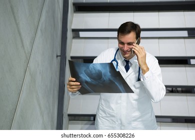 Male doctor discussing x-ray on mobile phone while walking downstairs in hospital - Powered by Shutterstock