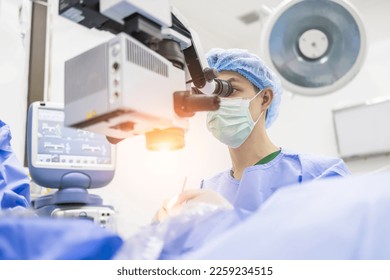 Male doctor doing surgery inside modern operating theater in surgical hospital.Microscope was use in eye surgery.Surgeon in blue sterile suit working with microscope with light effect.Medical concept.