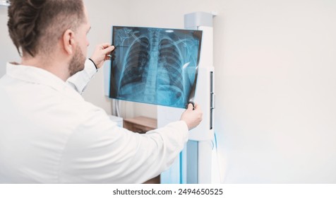 male doctor examines pictures of the lungs and ribs in the x-ray room, in the background x ray machine copy space - Powered by Shutterstock