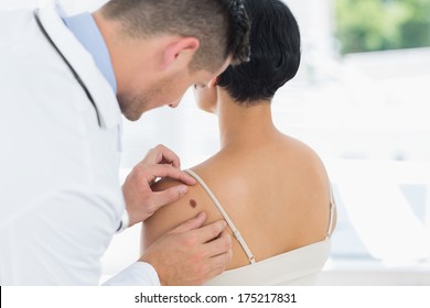 Male Doctor Examining Mole On Back Of Woman In Hospital