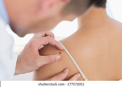 Male Doctor Examining Mole On Back Of Woman In Clinic