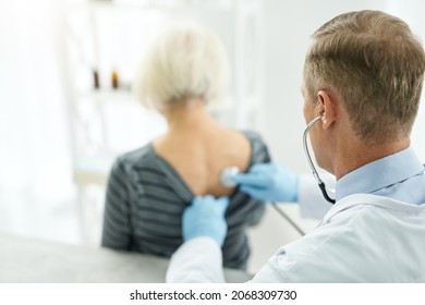 Male Doctor Examining Old Woman With Stethoscope In Clinic