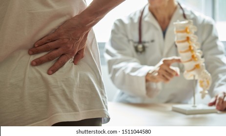 A male doctor explaining lumbar anatomy to female patient complaining of back pain at medical clinic - Powered by Shutterstock