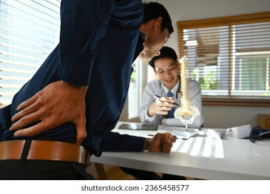 A male doctor explaining lumbar anatomy to a male patient complaining of back pain at a medical clinic, with Selective focus on patient. - Powered by Shutterstock