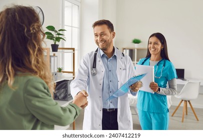 Male doctor with female nurse extend warm handshake to a patient in the hospital. Gesture epitomizes the commitment of the medical team. Physician consultation woman patient and sharing good results.