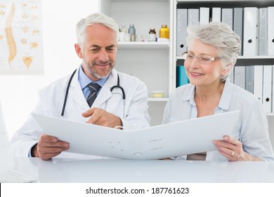 Male Doctor With Female Patient Reading Reports At Medical Office