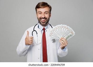 Male Doctor Fun Man Wears White Medical Gown Suit Work In Hospital Hold Fan Of Cash Money In Dollar Banknotes Show Thumb Up Isolated On Plain Grey Color Background Studio. Healthcare Medicine Concept