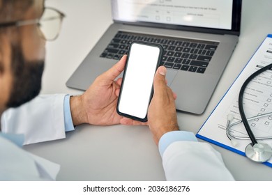 Male Doctor Gp Physician Holding Mobile Cell Phone In Hands Looking At White Blank Empty Mockup Smartphone Screen Working In Hospital. Ehealth Apps Technology Mock Up Concept. Over Shoulder View