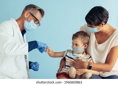 Male Doctor Greeting Small Patient With A Fist Bump. Doctor And Patient Wearing Face Masks During Pandemic.