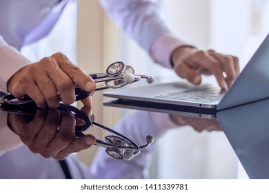 Male Doctor Hand Holding Stethoscope, Working And Typing On Laptop Computer Keyboard On The Desk At Clinic Or Hospital.Teleconference,telehealth, Online Medical,medic Tech,emr,ehr,telemedicine Concept