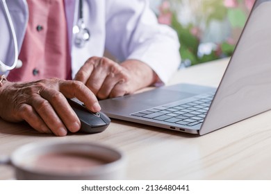 Male Doctor Hand Using Wireless Mouse, Browsing Medical Information On Laptop Computer With Stethoscope On The Desk. Online Internet Prescription Concept. 