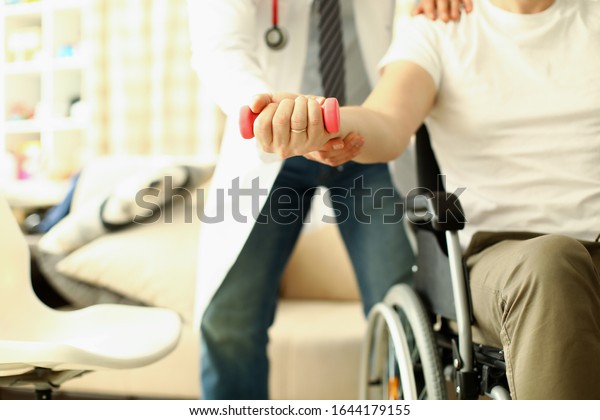 Male doctor helps lift dumbbell to disabled\
patient rehabilitation therapy concept. Process of recovering\
patients after severe\
injuries